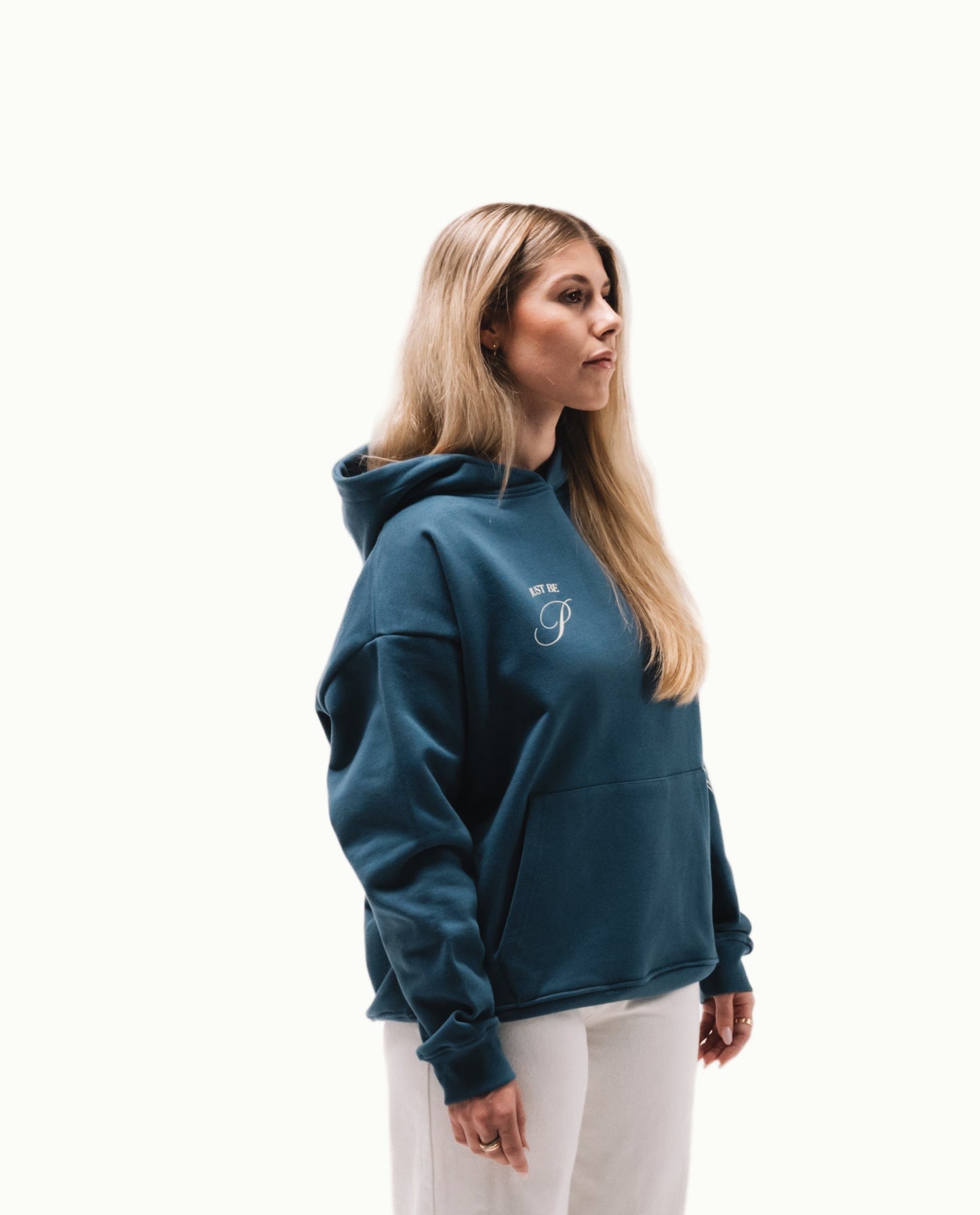 Modelo chica de perfil con sudadera Fly Different Hoodie azul petróleo y letras crema en pecho